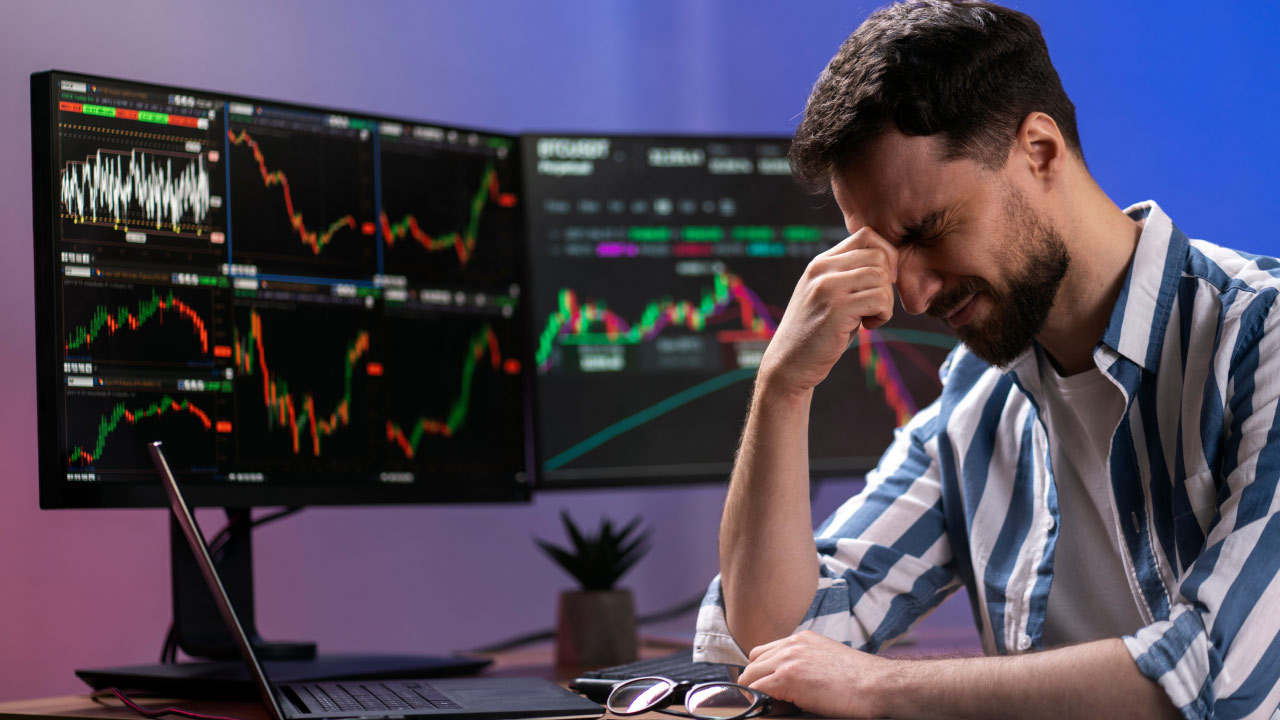 a frustrated male trader sitting at a desk with multiple computer monitors