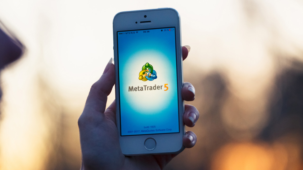 a hand holding a smartphone displaying the MetaTrader 5 loading screen