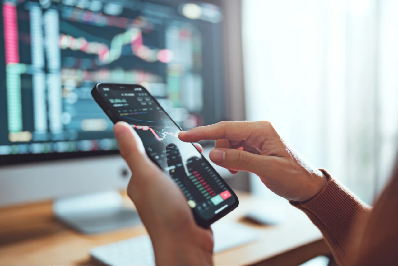 Correction or Recession? a mobile phone showing real-time trading charts with a hand navigating the trades, illustrating uncertainty in market conditions.