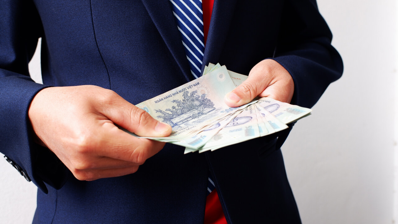 Common Mistakes When Exchanging Foreign Currency to Vietnamese Dong a person wearing a dark blue suit and striped tie holding and counting a stack of Vietnamese đồng banknotes, illustrating typical errors in currency exchange.