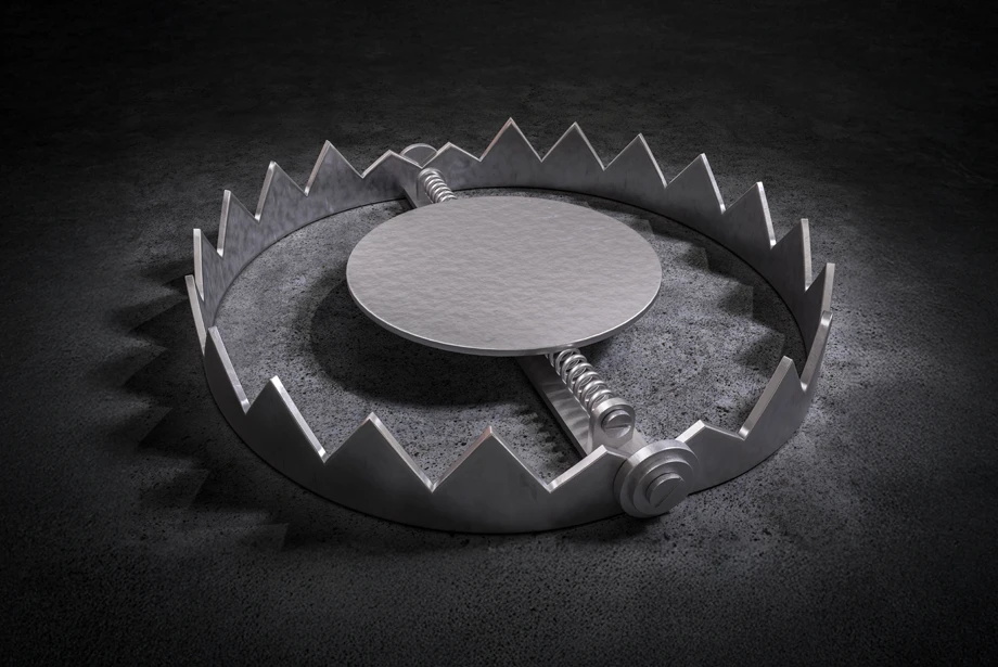 Metal bear trap with sharp jagged edges open on a dark textured floor, ready to snap shut.