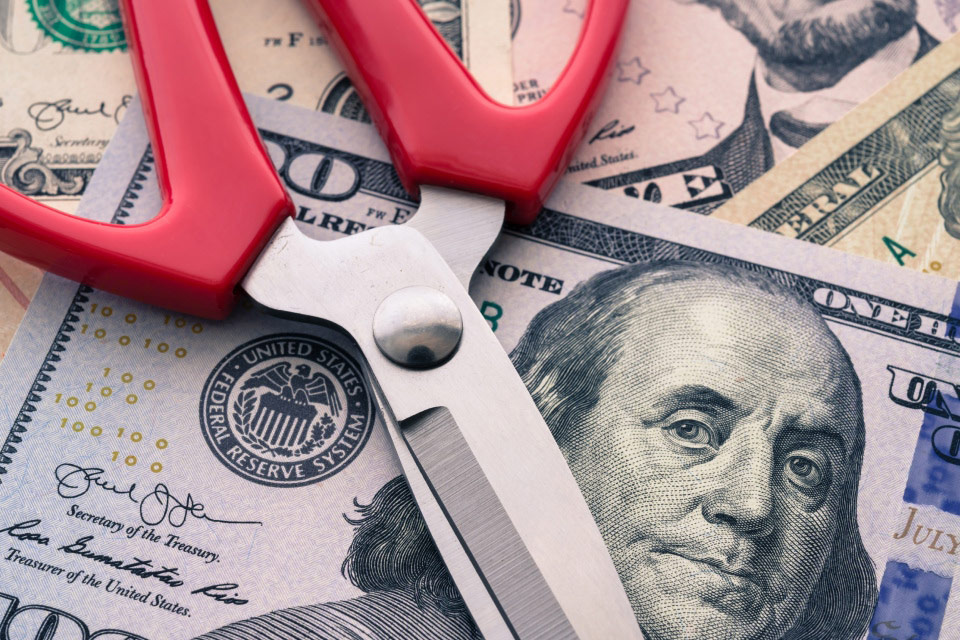 Scissors placed on US dollar bills, symbolizing interest rate cuts, illustrating the concept of what happens when a central bank cuts interest rates.