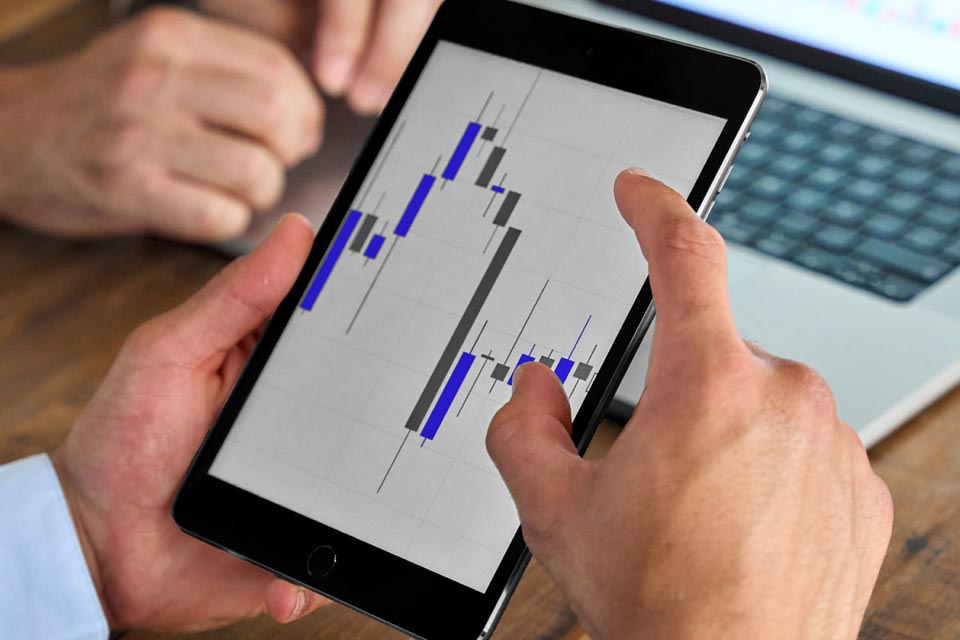 hands holding a tablet displaying candlestick chart patterns