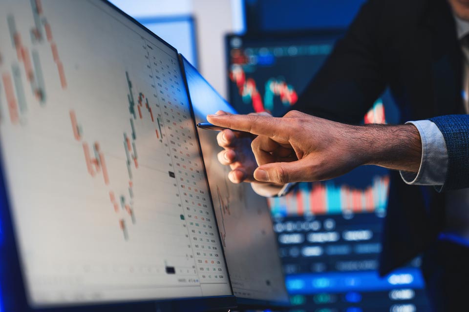 a close-up of a hand pointing at a computer monitor displaying technical trading charts