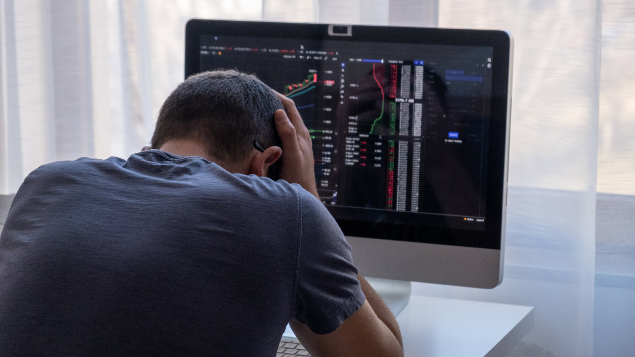 a frustrated trader with their head in their hands, sitting in front of a computer