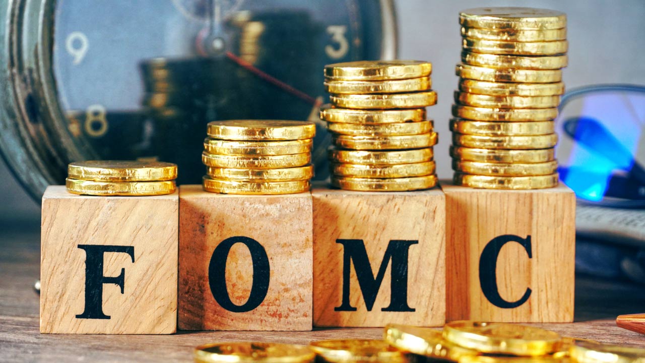 wooden blocks displaying the letters "FOMC" in front of stacks of gold coins