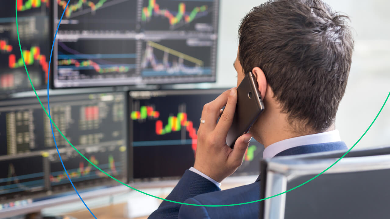 a trader in a suit talking on the phone while monitoring multiple financial charts