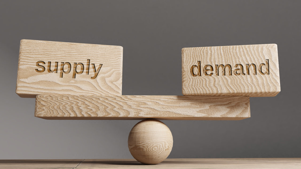 two wooden blocks labeled "supply" and "demand" are balanced on a wooden seesaw