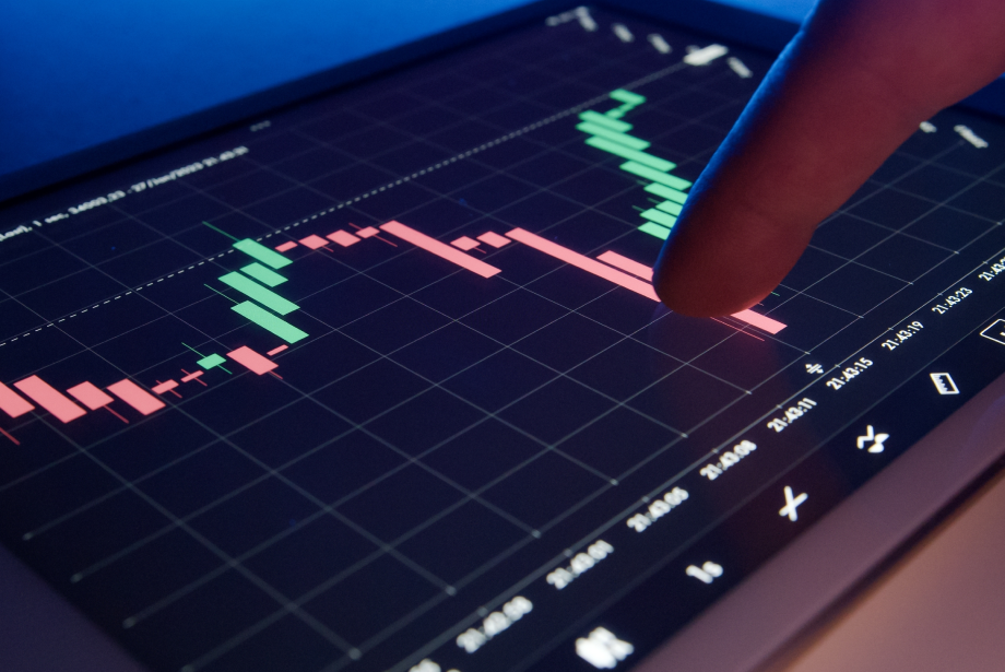 The image shows a tablet displaying a candlestick chart with green and red bars, with a finger pointing at the chart.