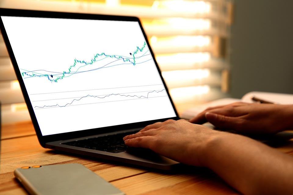 An image titled "What is The Oscillator of Moving Average in Forex?" showing a person analyzing forex trading charts on a laptop screen.