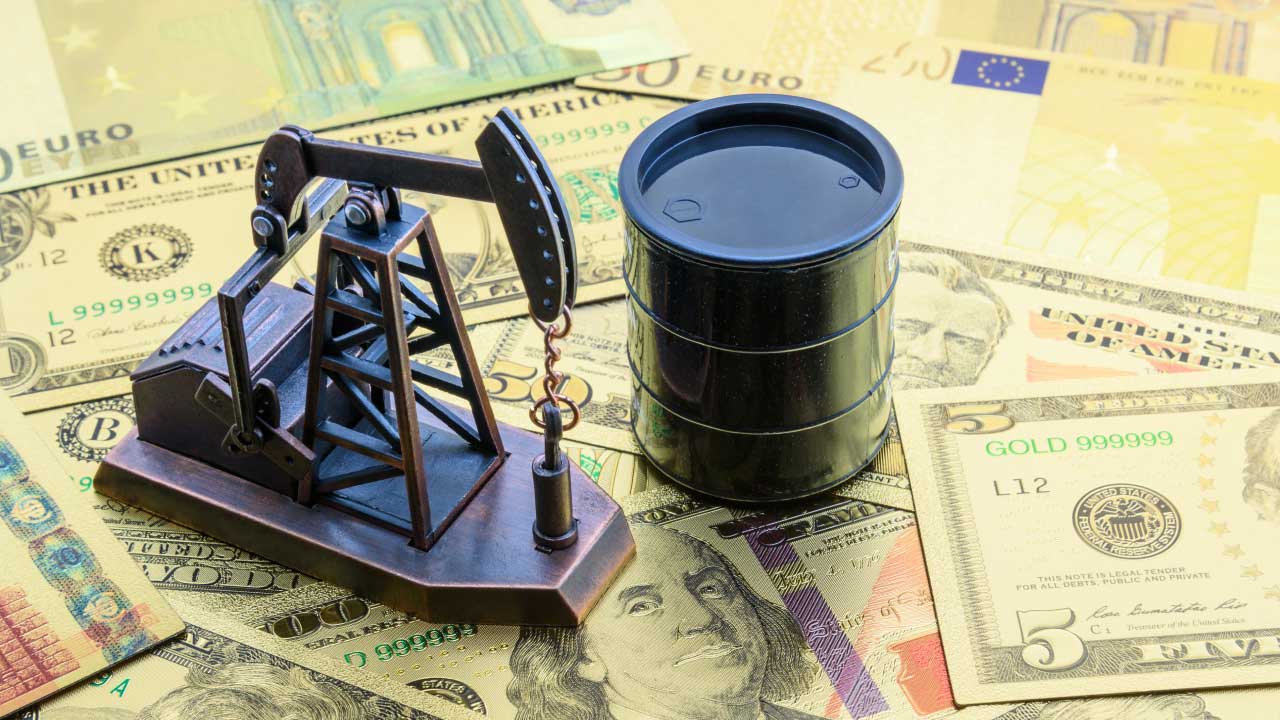 a miniature oil pump jack and a black oil barrel on top of different currencies