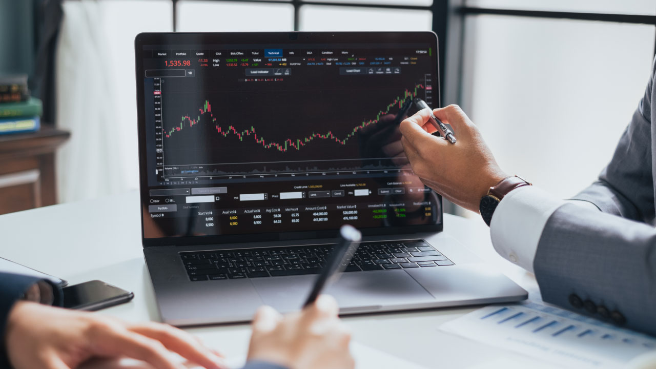 Two individuals in business attire analyzing a candlestick chart on a laptop screen, illustrating forex predictions 2024 and trends shaping the future of forex markets