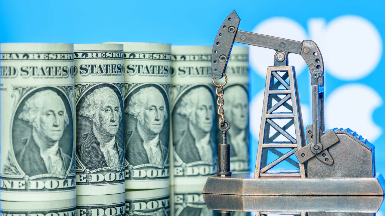 a miniature oil pump jack is placed in front of several rolled U.S. dollar bills