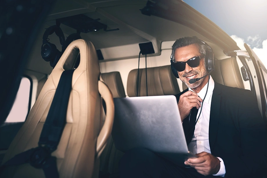 confident businessman wearing a headset and sunglasses working on a laptop inside a helicopter.