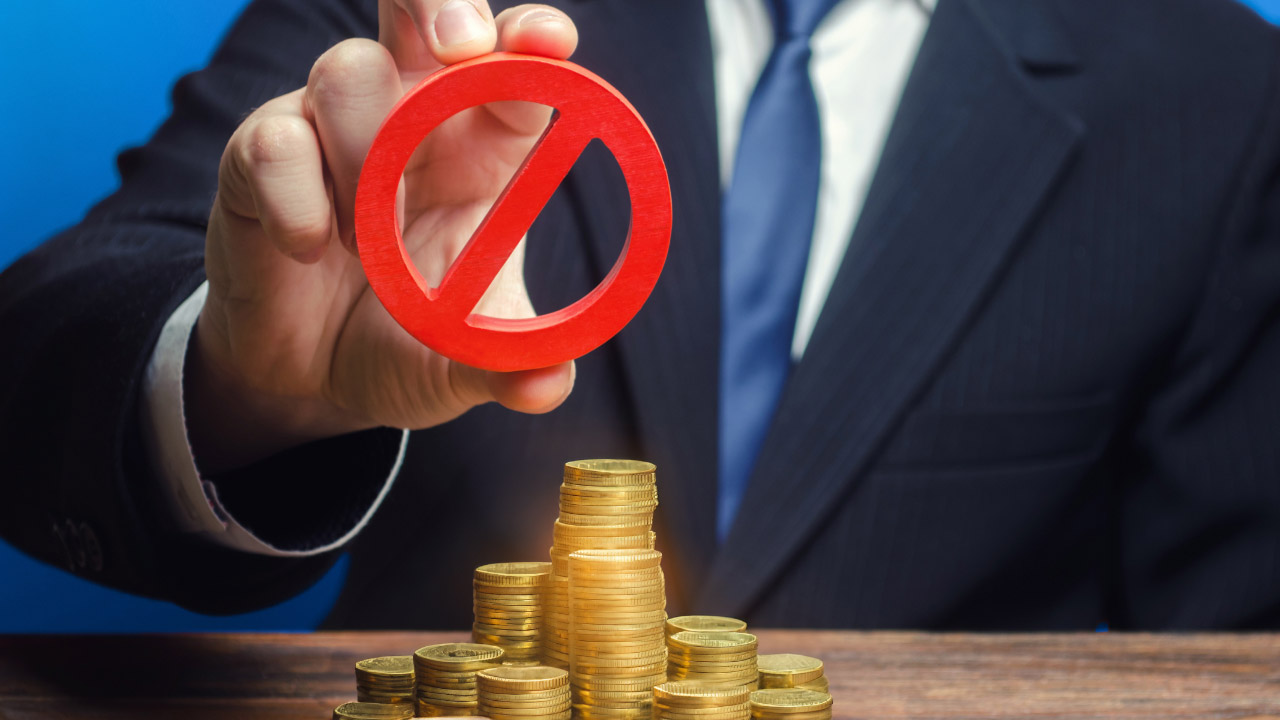 An image titled "4 Big Mistakes Traders Make When Setting Stops" featuring a man in a business suit holding a red prohibition symbol above a stack of gold coins.