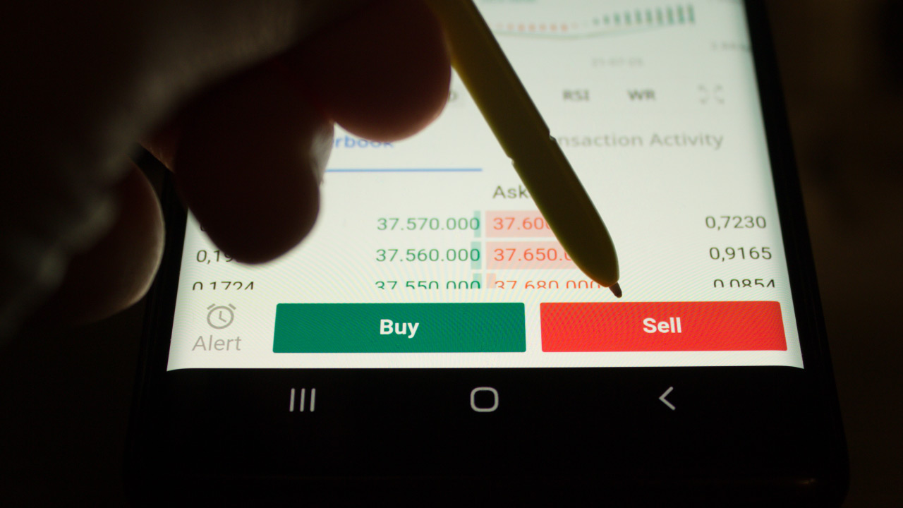 a mobile trading app screen showing the "Buy" and "Sell" options with a stylus