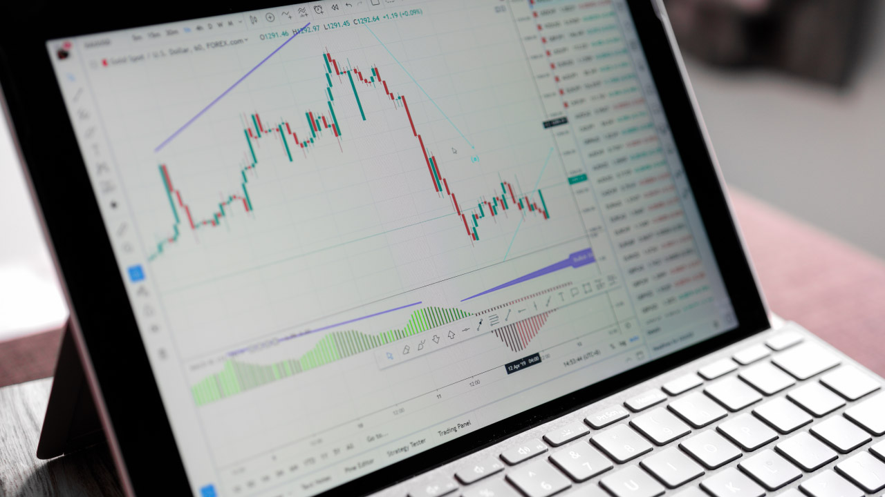 Close-up of a tablet on a keyboard stand showing a forex trading chart with candlestick patterns, illustrating practice using a forex demo account.