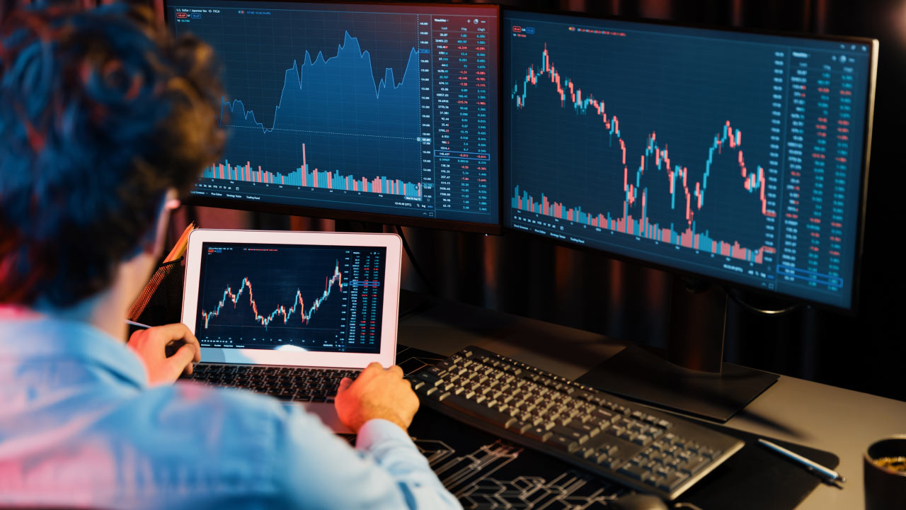 a trader analyzing financial charts on multiple screens in a dimly lit room