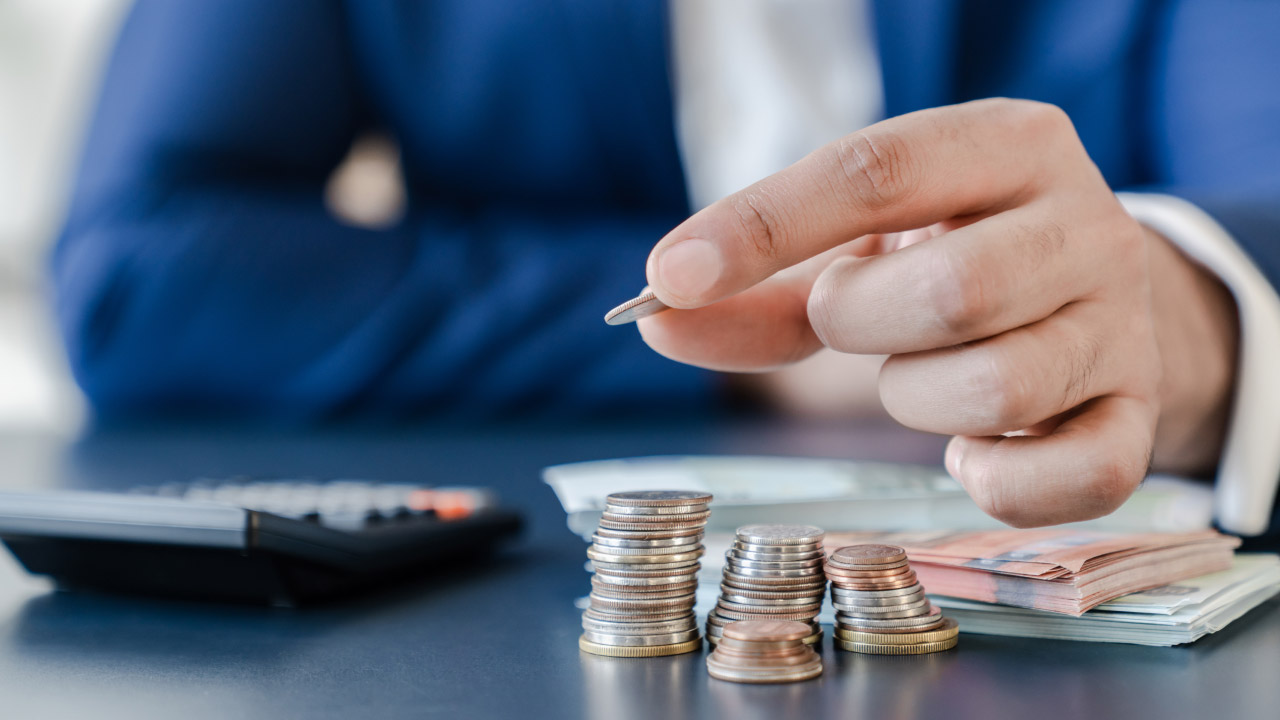 a businessperson in a blue suit counting coins with a calculator on the desk