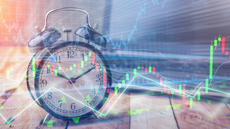 Alarm clock on a wooden surface overlaid with colorful forex trading candlestick charts and graphs