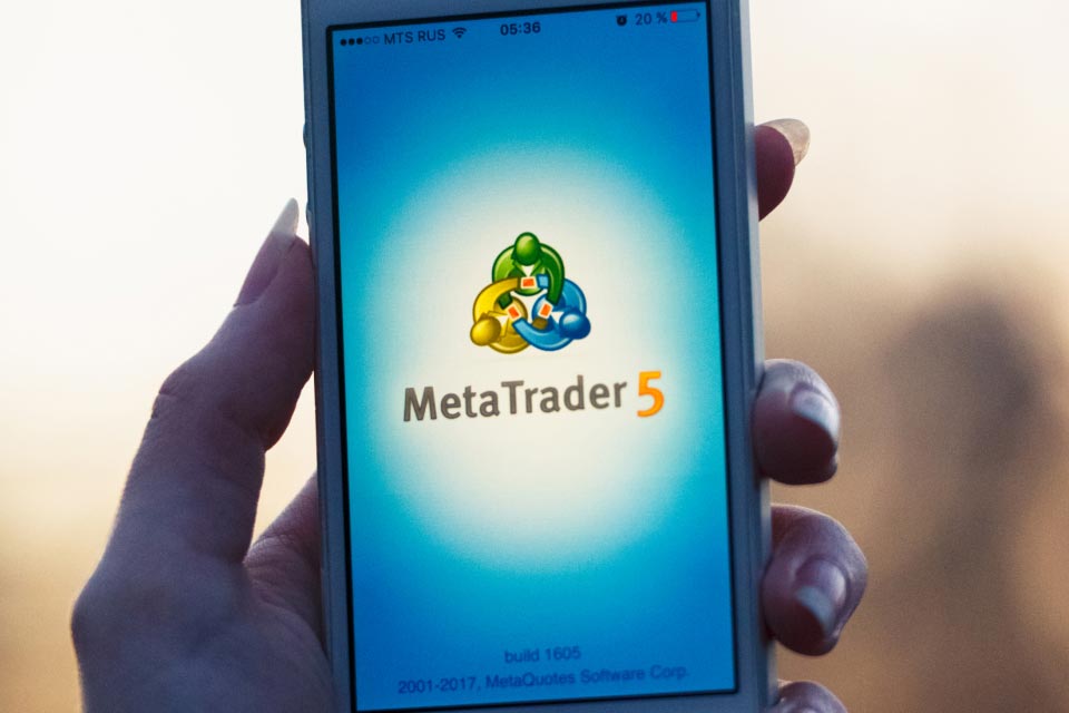 a hand holding a smartphone displaying the MetaTrader 5 logo on the screen