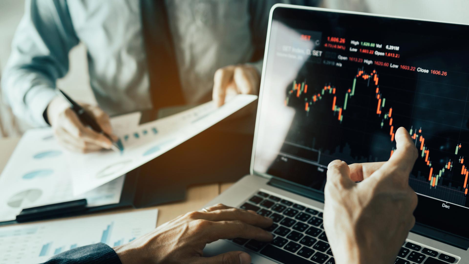 two professionals analyzing financial charts on a laptop and document