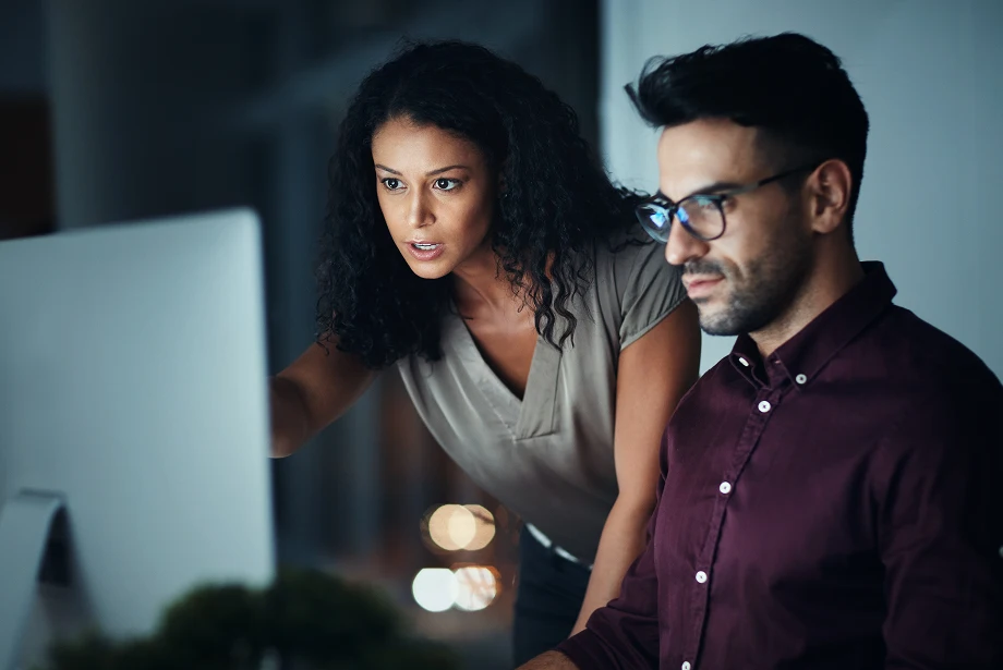 two colleagues collaborating on forex trading strategies while analyzing charts on a computer screen in a modern office.