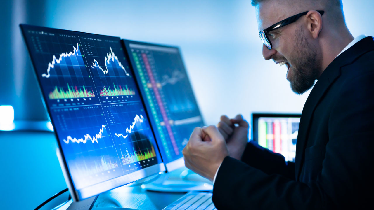 A man in front of his PC screen, thrilled by the results shown on charts and graphs, illustrating the importance of setting the right position sizing titled "How Setting The Right Position Sizing Can Save Traders?"