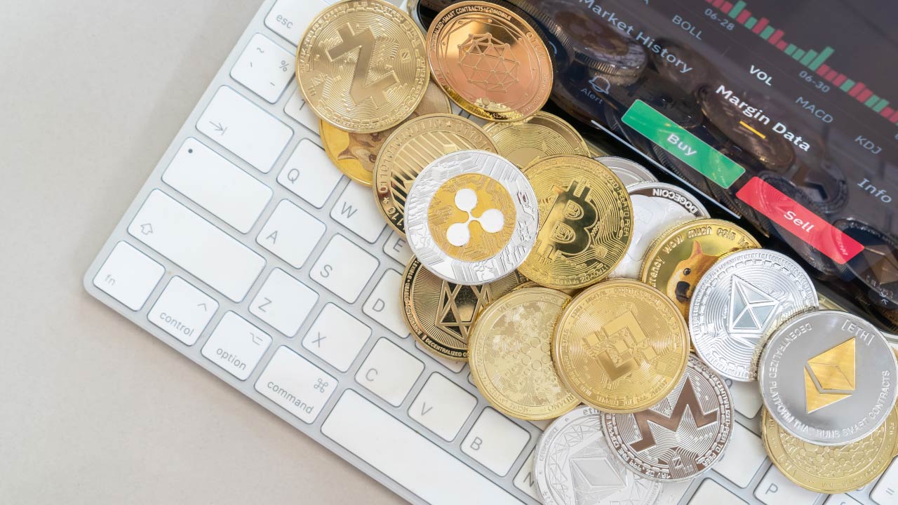 How to Invest in Crypto Without Buying Crypto? A collection of various physical cryptocurrency coins, including Bitcoin, Ethereum, Ripple, and Litecoin, placed on a white computer keyboard